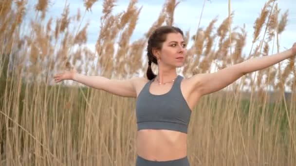 European woman doing yoga exercise on reed natural background. Concentrated girl training at summer outdoors. Pastel colors, unity with nature, balance, lifestyle concept. — Vídeo de Stock