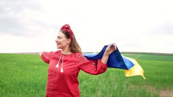 Happy ukrainian woman spinning around with national flag on sky background. Lady in red embroidery Vyshyvanka and flowers wreath. Ukraine freedom, patriot symbol, victory in war. — Stockvideo