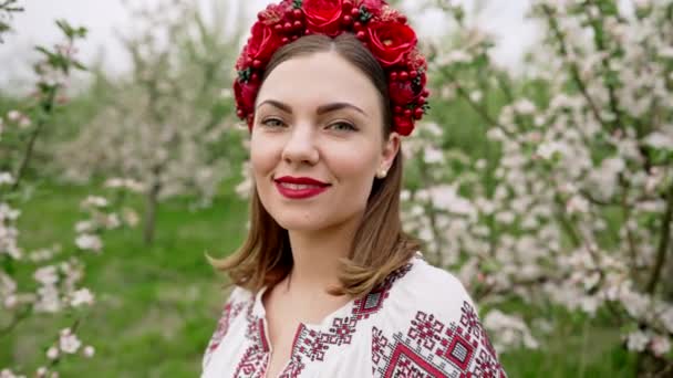 Joven mujer bonita en el vestido festivo tradicional vyshyvanka en el jardín de flores. Bordado ucraniano, traje nacional. Hermosa chica sonriente, alegre dama. — Vídeo de stock