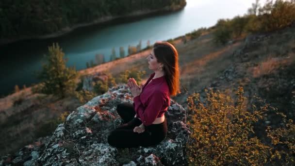 Concentrated woman in lotus pose doing meditation on high rock above water. Calm yoga concept, religion, zen, peaceful mind, practice on nature background. — Stockvideo
