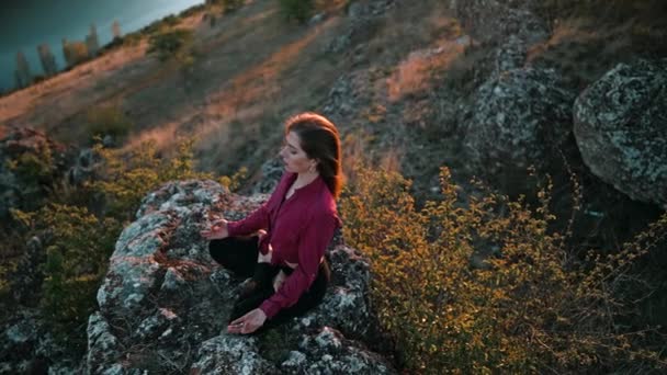 Nilüfer çiçekli genç, güzel bir Yogi kadın suyun üzerindeki yüksek kayalarda meditasyon yapıyor. Sakin yoga konsepti, din, zen, barışçıl zihin, doğa arka planı üzerine uygulama. — Stok video