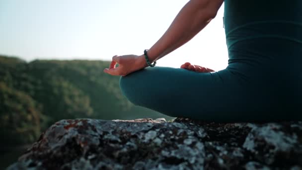 Healthy woman sitting in lotus pose and meditating on high cliff above river. Calm yoga concept, zen, relaxation, practice on nature background. — Stock video