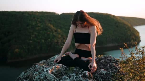 Young woman doing yoga belly exercise - Kapalabhati yogic breathing technique.Yogi does uddiyana bandha, while sitting in lotus pose on high cliff above water outdoors.Lady breathing and meditating — Stockvideo