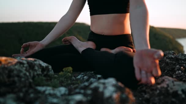 Young woman doing yoga belly exercise - Kapalabhati yogic breathing technique. Yogi detoxtechnique while sitting in lotus pose on high cliff above water outdoors. Lady slows breathing and meditating. — Vídeo de Stock