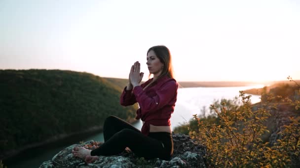 Yogi woman doing yoga exercise on top of cliff. Concentrated girl training at breathing while sitting in lotus pose. Unity with nature, meditation, balance, healthy lifestyle concept. — Stock Video