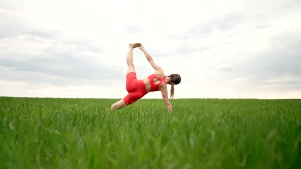 Strong woman in orange wear doing yoga Vasishthasana Side Plank in green field. Girl building strong core, focused and motivated. Fitness, everyday practice on nature, healthy lifestyle concept. — Αρχείο Βίντεο