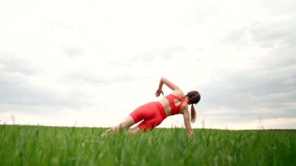 Strong woman in orange wear doing yoga Vasishthasana Side Plank in green field. Girl building strong core, focused and motivated. Fitness, everyday practice on nature, healthy lifestyle concept.