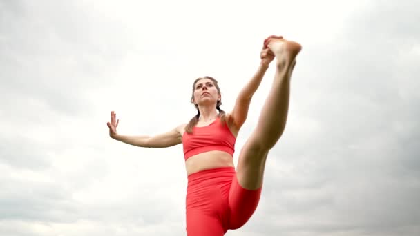 Žena v oranžovém sportovním oblečení cvičit jógu - utthita hasta padangushthasana v zeleném poli. Rovnováha na jedné noze. fitness, sport, zdravý životní styl. — Stock video