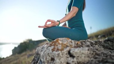 Mavi tulumlu genç bayan rahatlıyor, dışarıda yoga yapıyor, ellerin yakın çekimi, gyan mudra ve lotus pozu. Dolly vurdu. Sağlıklı yaşam tarzı, derin nefes al, parlak akıl kavramı.