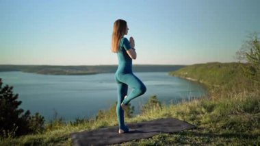 Vriksasana 'da pratik yapan kadın, ağaç pozu, yüksek dağda su üstünde yoga yapan kadın. Meditasyon. Doğada esneklik egzersizi. Güçlü bayan dengede çalışıyor. Sağlıklı yaşam tarzı.