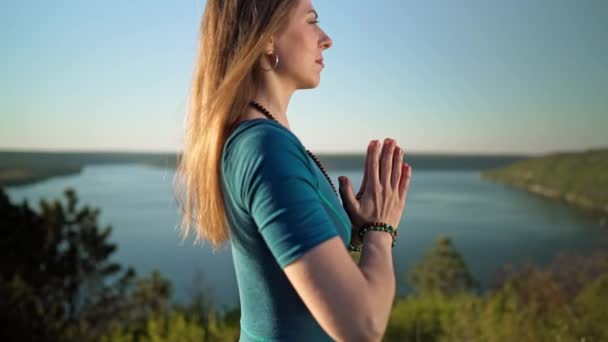 Femme pratiquant le yoga, namaste gratitude mudra seul sur la haute montagne au-dessus de la rivière en été. Une fille en salopette bleue. Religion, pureté, résignation, concept de spiritualité. — Video