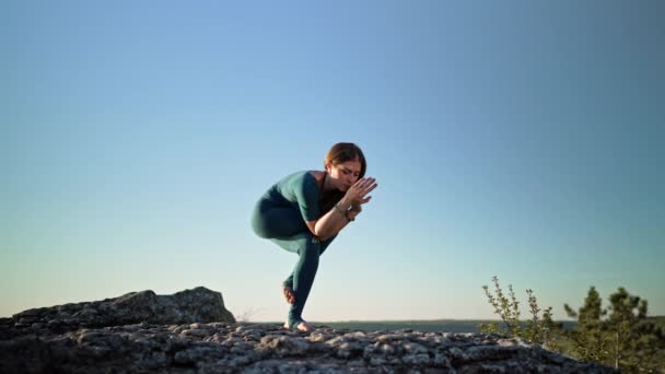 Vrouw oefenen in Garudasana - adelaar pose, yoga op hoge berg boven water. Flexibiliteit training op de achtergrond van de natuur. Sterke dame die nek en rug versterkt — Stockvideo