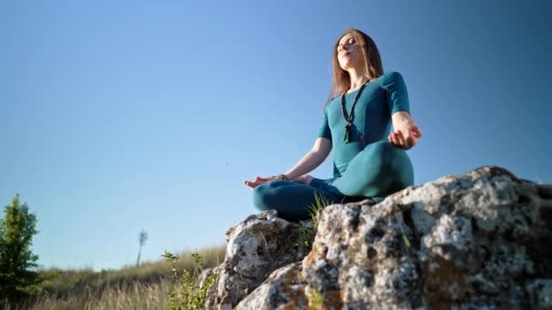 Mulher concentrada em lótus posar fazendo meditação em penhasco alto acima da água. Calmo conceito de ioga, religião, zen, mente pacífica, prática no fundo da natureza. — Vídeo de Stock