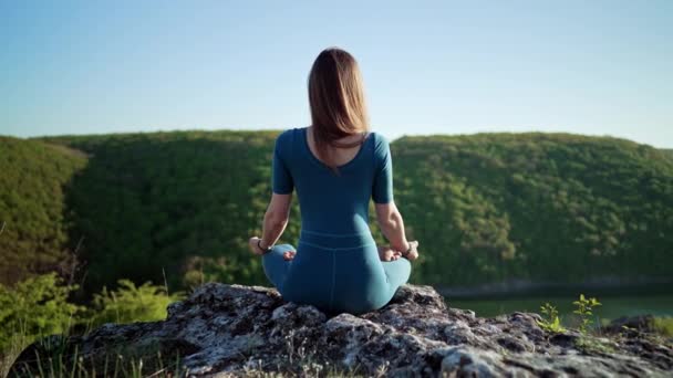 Concentrated woman in lotus pose doing meditation on high cliff above water. Calm yoga concept, religion, zen, peaceful mind, practice on nature background. — Stock Video