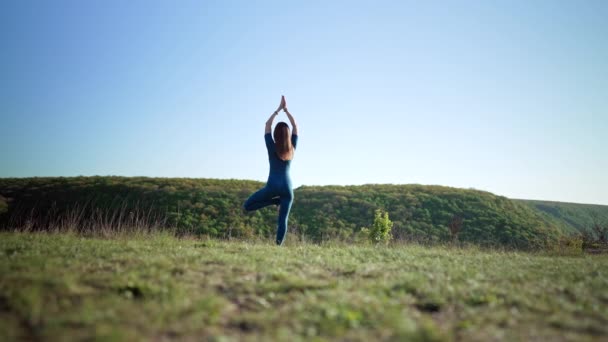 Cvičení žen ve Vriksasaně - póza stromu, jóga na vysokém kopci. Meditace. Flexibilita cvičení na přírodním pozadí. Silná dáma trénuje v rovnováze. Zdravý životní styl. — Stock video