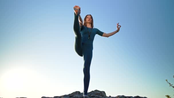 Donna in tuta blu praticare yoga - utthita hasta padangushthasana su sfondo cielo blu. Equilibrio su una gamba. fitness, sport, stile di vita sano. — Video Stock