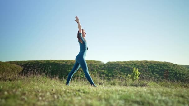 Femme en bleu vêtements de sport pratiquant le yoga penche vers l'avant, équilibre sur la haute montagne, fond de la nature. Fitness, sport, mode de vie sain concept. — Video