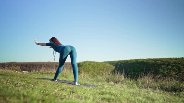 Женщина в синей спортивной одежде практикует йогу - наклоняется вперед, балансирует на высоких горах, на природном фоне. Фитнес, спорт, концепция здорового образа жизни. — стоковое видео