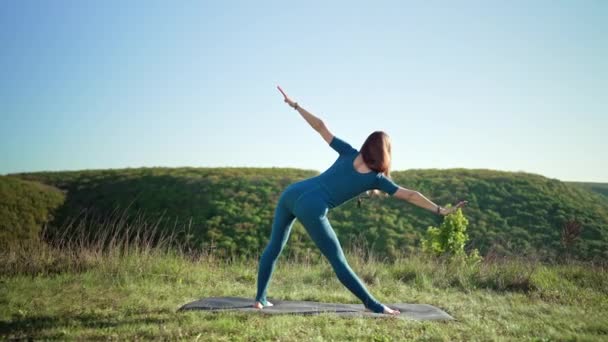 Femme en bleu vêtements de sport pratiquant le yoga penche vers l'avant, équilibre sur la haute montagne, fond de la nature. Fitness, sport, mode de vie sain concept. — Video