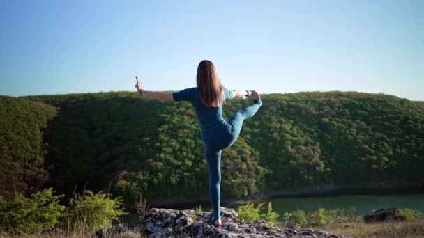 Donna in tuta blu praticare yoga utthita hasta padangushthasana sulla scogliera alta sopra l'acqua. Equilibrio su una gamba. fitness, sport, stile di vita sano. — Video Stock