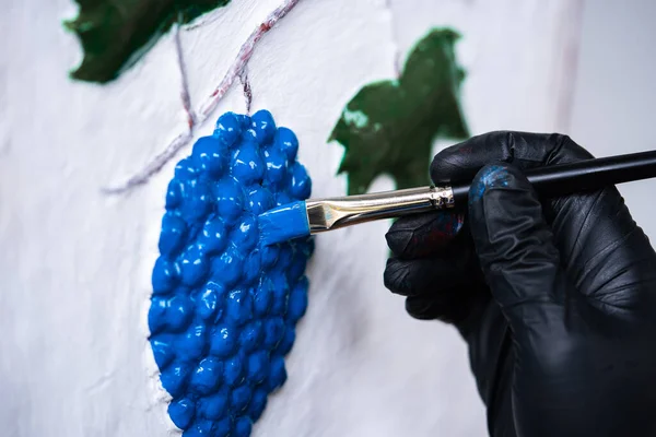 アーティストの作品は、青の塗料でブラシでブドウを着色。絵画の道具。ウクライナの村の家の伝統的なパターンの装飾 — ストック写真