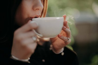Beyaz porselen bardaktan kahve içen kadın. Kahve makinesinden köpükle taze sıcak içkinin tadını çıkaran bir bayan. Kafein, enerji, aroma kavramı