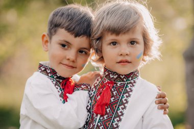 Yanaklarında mavi bayrak resmi olan gülümseyen küçük Ukraynalı çocuklar. Geleneksel işlemeli vyshyvanka tişörtlü çocuklar. Ukrayna, kardeşler, özgürlük, ulusal kostüm, savaşta zafer.