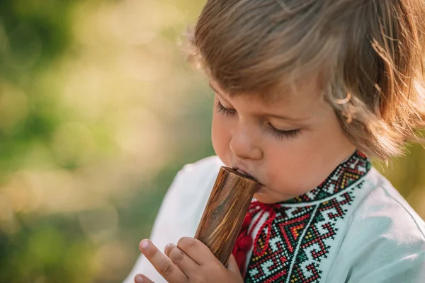 Uroczy chłopiec grający na drewnianym flecie - ukraińskiej sopilce. Koncepcja muzyki ludowej. Instrumenty muzyczne. Dziecko w tradycyjnej koszuli haftowanej - Vyshyvanka. — Zdjęcie stockowe