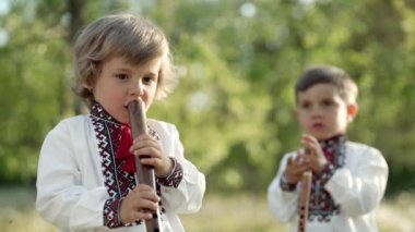 Küçük kardeşler tahta flüt çalıyorlar. Ukraynalı sopilka açık havada. Halk müziği konsepti. Müzik aleti. Geleneksel işlemeli gömlekli çocuklar - vyshyvanka.