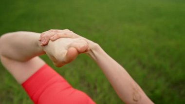 Turuncu spor dalında tanınmayan yoga yapan, yeşil alanda gerinen bir Yogi kadını. Karmaşık asanalar, bacak esnetme, esneklik.