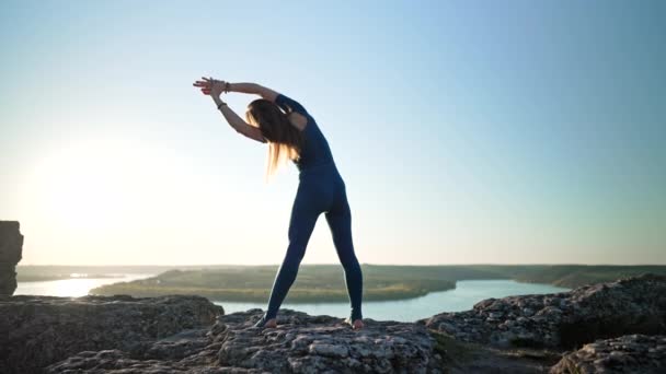 Silueta de mujer yogui comenzando la práctica de yoga en la cima de la roca en alta montaña. Naturaleza salvaje, humano libre. Libertad, flexibilidad, práctica diaria, estiramiento corporal — Vídeo de stock