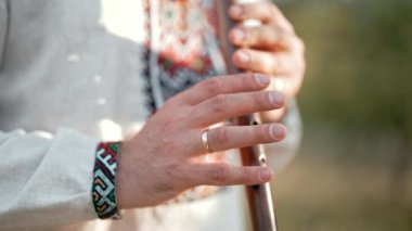 Ahşap flüt çalan genç adamın elleri. Ukraynalı sopilka açık havada. Halk müziği konsepti. Müzik aleti. Geleneksel nakışlı gömlekli müzisyen - Vyshyvanka.