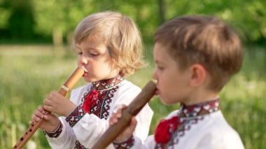 Küçük kardeşler tahta flüt çalıyorlar. Ukraynalı sopilka açık havada. Halk müziği konsepti. Müzik aleti. Geleneksel işlemeli gömlekli çocuklar - vyshyvanka.