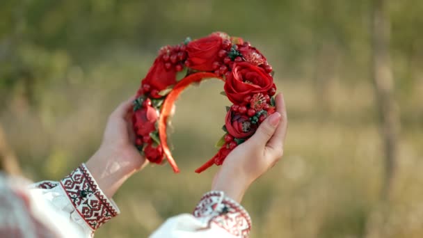 Украинка держит в руках венок из красных цветов и вибурнума. Она восхищается ее традиционным украшением головы — стоковое видео