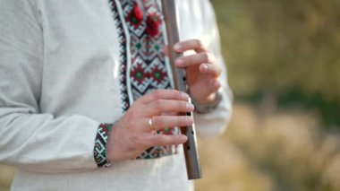 Ahşap flüt çalan genç adamın elleri. Ukraynalı sopilka açık havada. Halk müziği konsepti. Müzik aleti. Geleneksel nakışlı gömlekli müzisyen - Vyshyvanka.