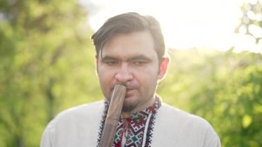 Ahşap flüt çalan genç adam - Ukrayna sopilkası açık havada. Halk müziği konsepti. Müzik aleti. Geleneksel nakışlı gömlekli müzisyen - Vyshyvanka.