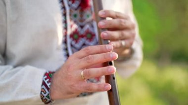 Ahşap flüt çalan genç adamın elleri. Ukraynalı sopilka açık havada. Halk müziği konsepti. Müzik aleti. Geleneksel nakışlı gömlekli müzisyen - Vyshyvanka.