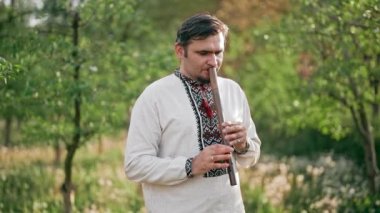 Ahşap flüt çalan genç adam - Ukrayna sopilkası açık havada. Halk müziği konsepti. Müzik aleti. Geleneksel nakışlı gömlekli müzisyen - Vyshyvanka.