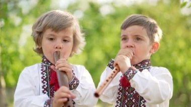Küçük kardeşler tahta flüt çalıyorlar. Ukraynalı sopilka açık havada. Halk müziği konsepti. Müzik aleti. Geleneksel işlemeli gömlekli çocuklar - vyshyvanka.