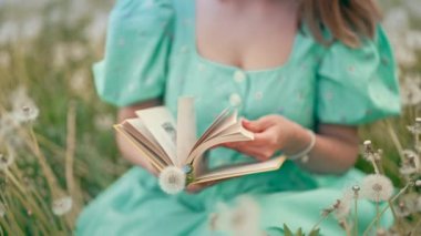 Kadının elleri eski kâğıt kitapların sayfalarını çeviriyor. Retro ya da klasik elbise giyen bir kadın doğanın üzerine otururken ilginç bir roman okuyor. Atmosferik sahne. Eğitim, bilim, üniversite konsepti. 4k görüntü