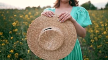 Elinde siyah kurdeleli saman şapka tutan bir kadın. Yazın kanola sahasında duran ve klasik bir tekne gezisi yapan bir kız. Yüksek kalite 4k görüntü