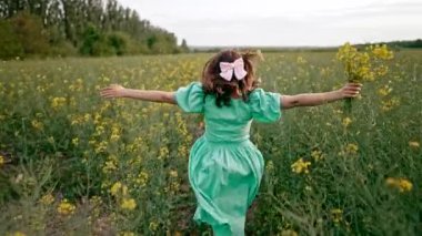 Çiçek açan kanola çiçeklerinin arasında koşan genç bir kadın, inanılmaz olumlu görüntüler. İlkbaharda doğa mekanında romantik ve özgür bir kadın. Yüksek kalite 4k görüntü