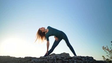 Yogi kadın yoga yapıyor - Trikonasana yüksek dağdaki kayanın tepesinde. Vahşi doğa, özgür insan. Özgürlük, esneklik, günlük çalışma, vücut germe. Yüksek kalite 4k görüntü