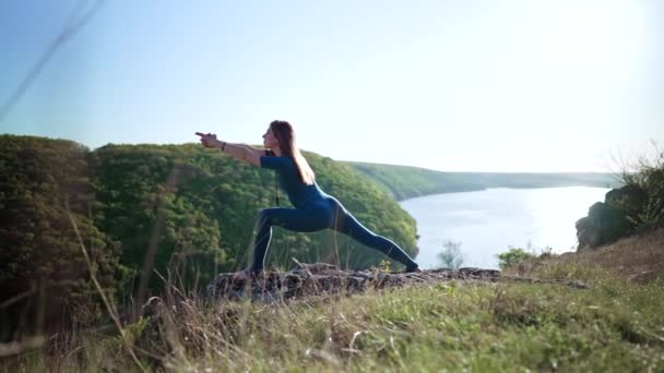 青いスポーツウェアを着てヨガを練習する女性 Virabhadrasana 高い山の上でバランス 自然背景 フィットネス スポーツ 健康的なライフスタイルのコンセプト 高品質4K映像 — ストック動画