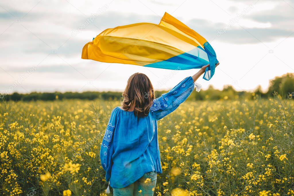 Ukrainian patriot woman waving national flag in canola yellow field. Rare, back view. Ukraine unbreakable, peace, independence, freedom, victory in war. High quality photo