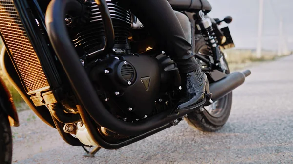 Klasik bisikletin üzerinde oturan şık motosikletli kadının bacakları. Siyah eski model motosiklet. Yepyeni bir motosikletin klasik tasarımının ayrıntıları. Güneş parlaması, açık havada. Yüksek kalite fotoğraf