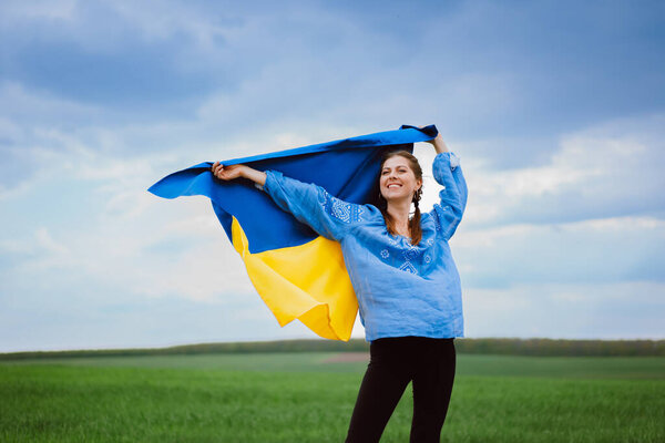 Happy free ukrainian woman with national flag on dramatic sky background. Portrait of lady in blue embroidery vyshyvanka shirt. Ukraine, independence, patriot symbol. High quality photo