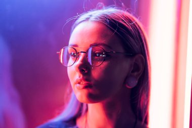 Bin yıllık gizemli güzel kızla gece parlak neon duvarının yakınında alışılmadık boyalı saç modeli. Saç, altın pullu çiller olarak mavi, piercing burun. Gizemli hipster genç gözlük.