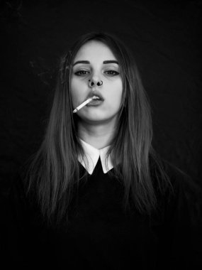 Emo girl smoking cigarette. Young student or pupil with blue colorful dyed hair, hat, piercing,lenses,ears tunnels and unusual hairstyle stands on black background.