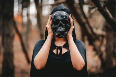 Witch woman in black clothes holds skull at level of her head. Death Eater concept, Halloween, horror, scary symbol of dead. High quality photo